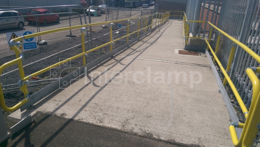 Interclamp Key Clamp DDA Assist fittings combined with safety yellow powder-coated handrail tube to create a compliant disabled access ramp at a train station, providing essential support.